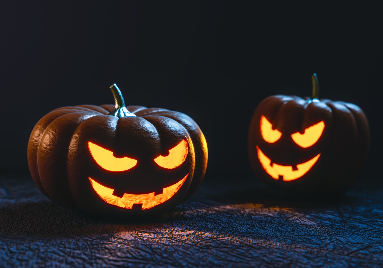 Two humorously evil jack-o-lantern pumpkins at night with yellow glowing eyes and smiles