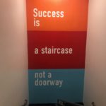 "Success is a staircase not a doorway" wall mural installation on wall behind inner stairway landing for Mission Fed Credit Union