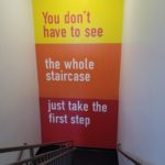 "You don't have to see the whole staircase. Just take the first step" Wall Mural installation on interior stairway wall behind landing for Mission Federal Credit Union