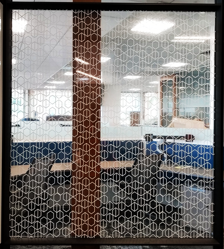 intricate angular geometric pattern in thin white lines printed on clear window film installed on interior office window.