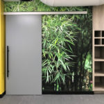 Wall mural of bamboo leafs on interior wall beside security door.