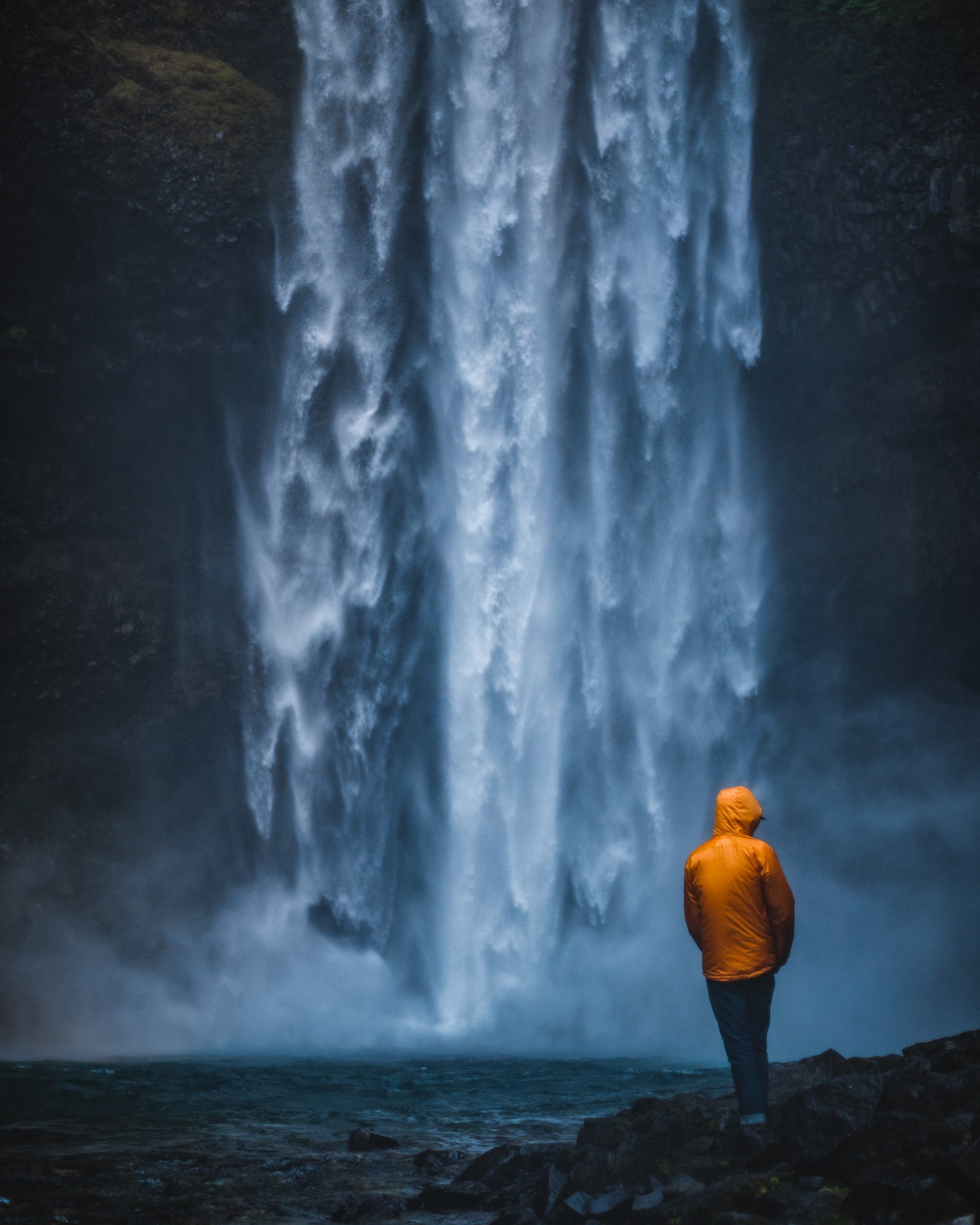 dark waterfall with yellow raincoat-clad figure before it